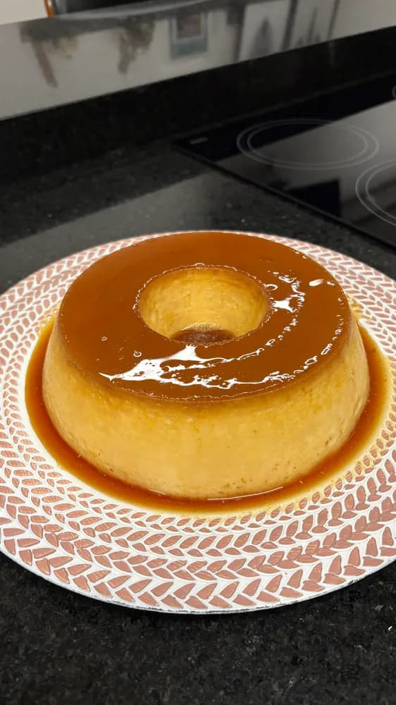 Pudim de leite com calda de caramelo em prato branco sobre bancada escura