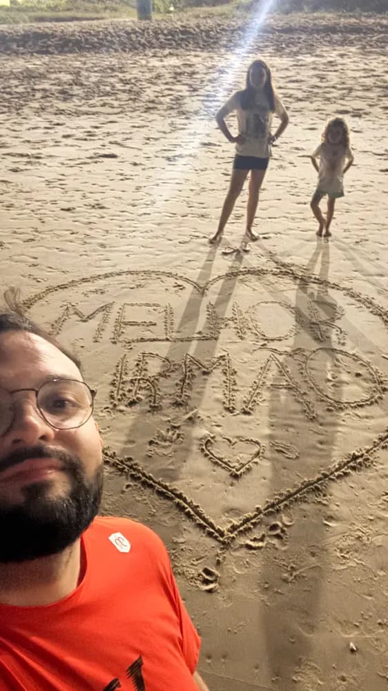 Selfie na praia, 'melhor irmão' escrito na areia e duas crianças ao fundo