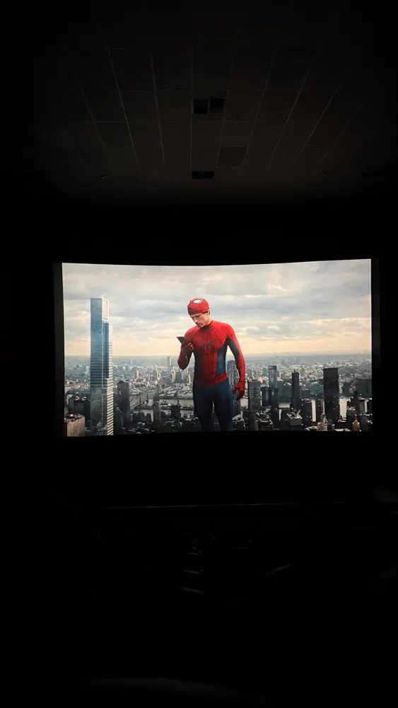 Sala de cinema escura, tela com um herói de uniforme vermelho e azul