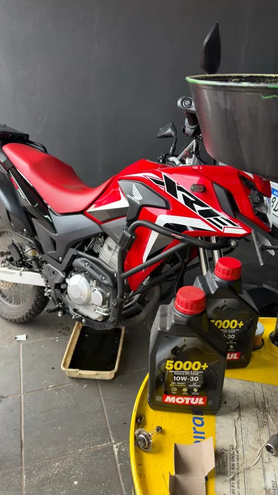 Moto vermelha em troca de óleo, frascos de lubrificante e bandeja no chão