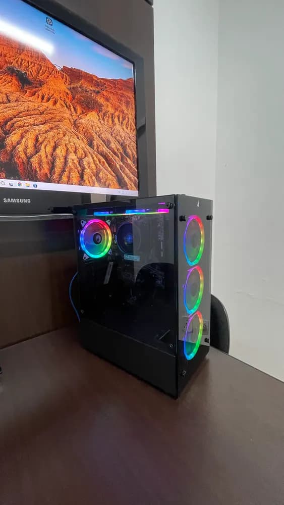 Gabinete de PC com coolers RGB acesos na mesa, ao lado de um monitor