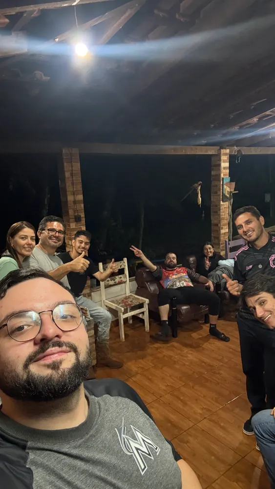 Amigos sentados numa varanda à noite, sob lâmpada e telhado de madeira