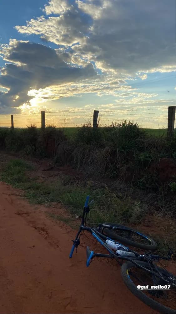 Bicicleta deitada numa estrada de terra vermelha, pôr do sol sobre o campo
