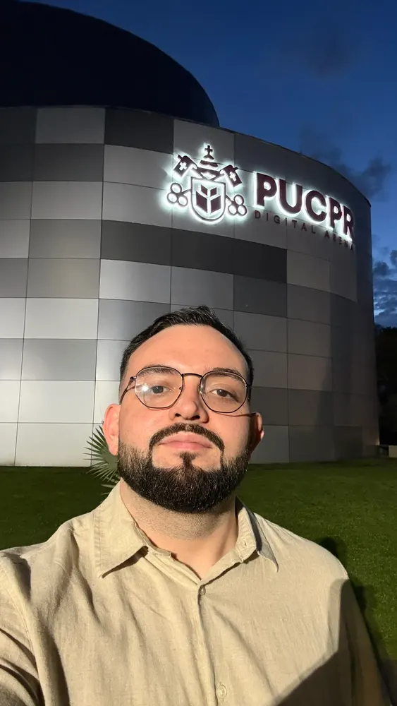 Selfie de um homem de óculos à noite, diante da PUCPR Digital Arena