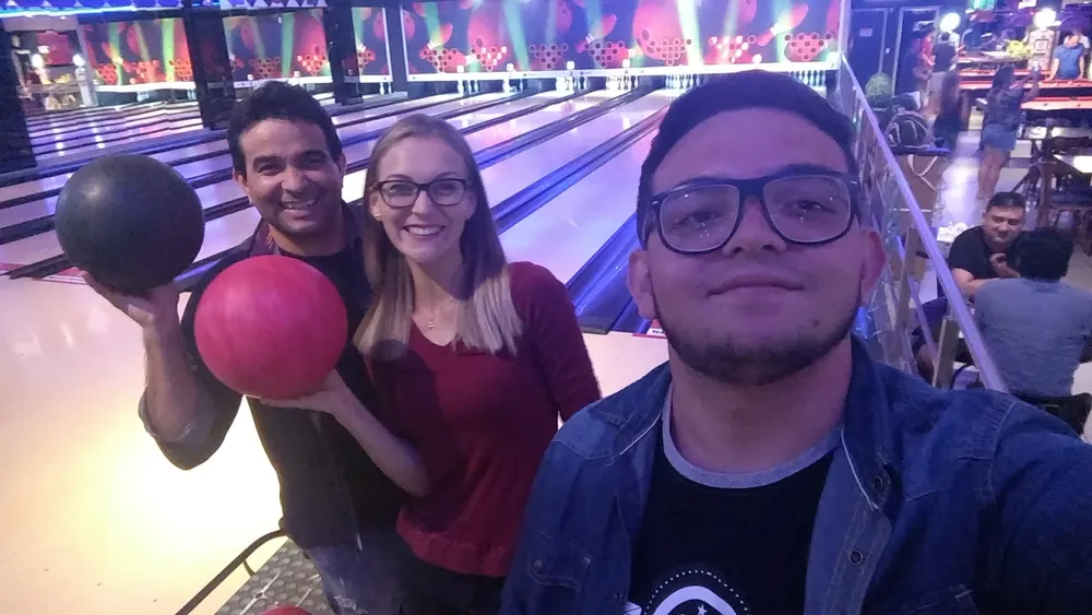 Selfie de três amigos numa pista de boliche, dois segurando bolas