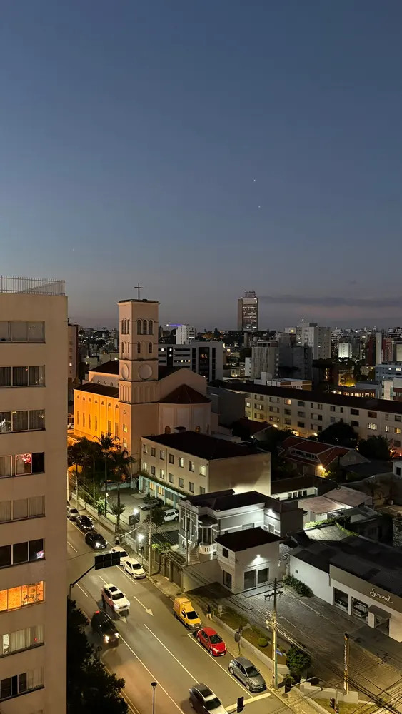 Vista do alto da cidade ao anoitecer, igreja iluminada e avenida com carros