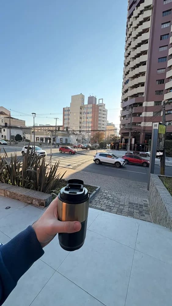 Mão segurando copo térmico diante de rua com carros e prédios altos