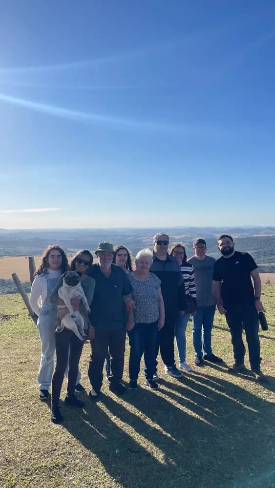 Família reunida em morro gramado com vale ao fundo, um segura cachorro