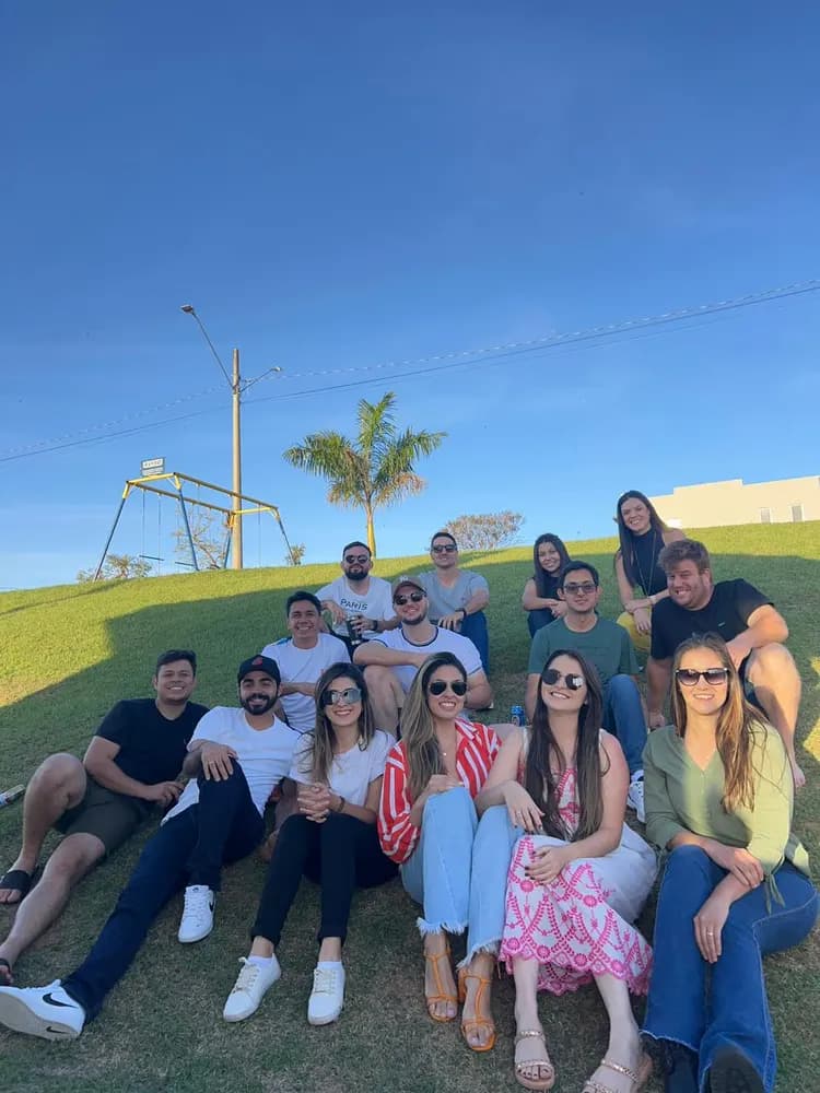 Grupo grande de amigos sentado na grama, balanço e céu azul ao fundo