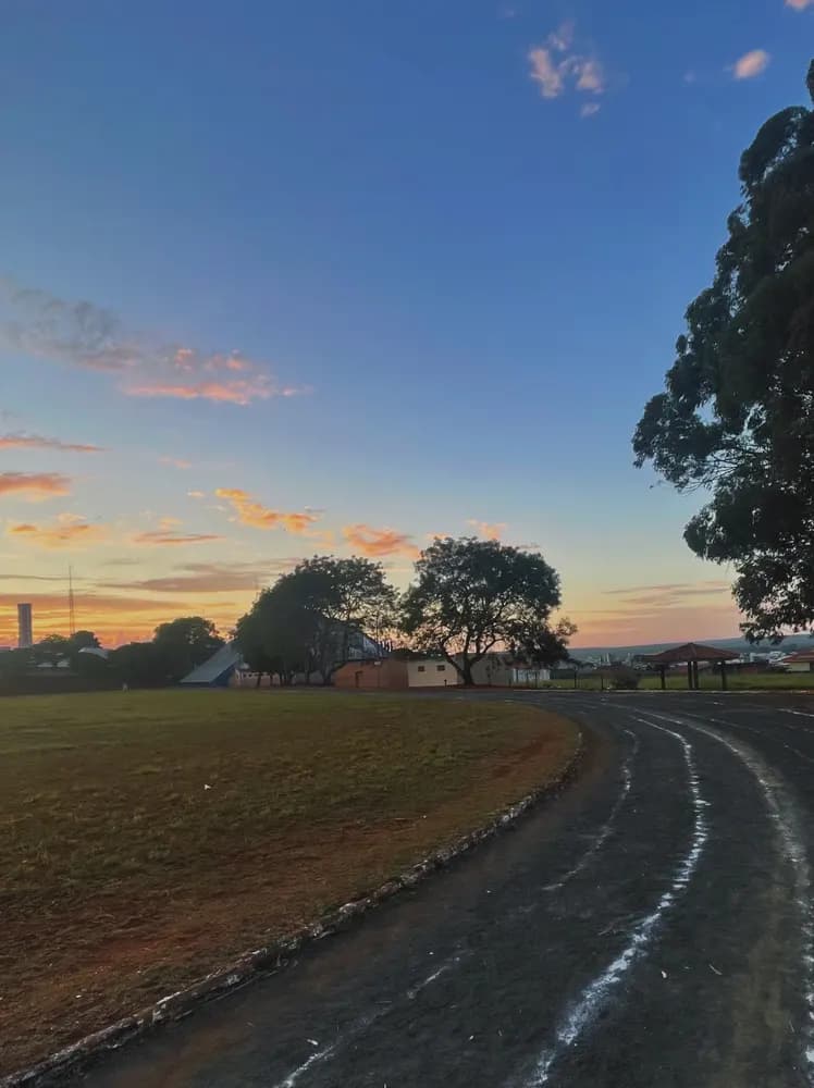 Pista de terra com raias brancas contornando um campo gramado ao pôr do sol