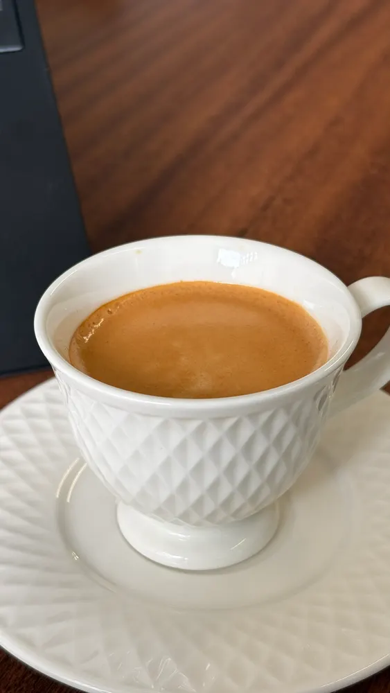 Xícara branca com café sobre pires, em mesa de madeira escura