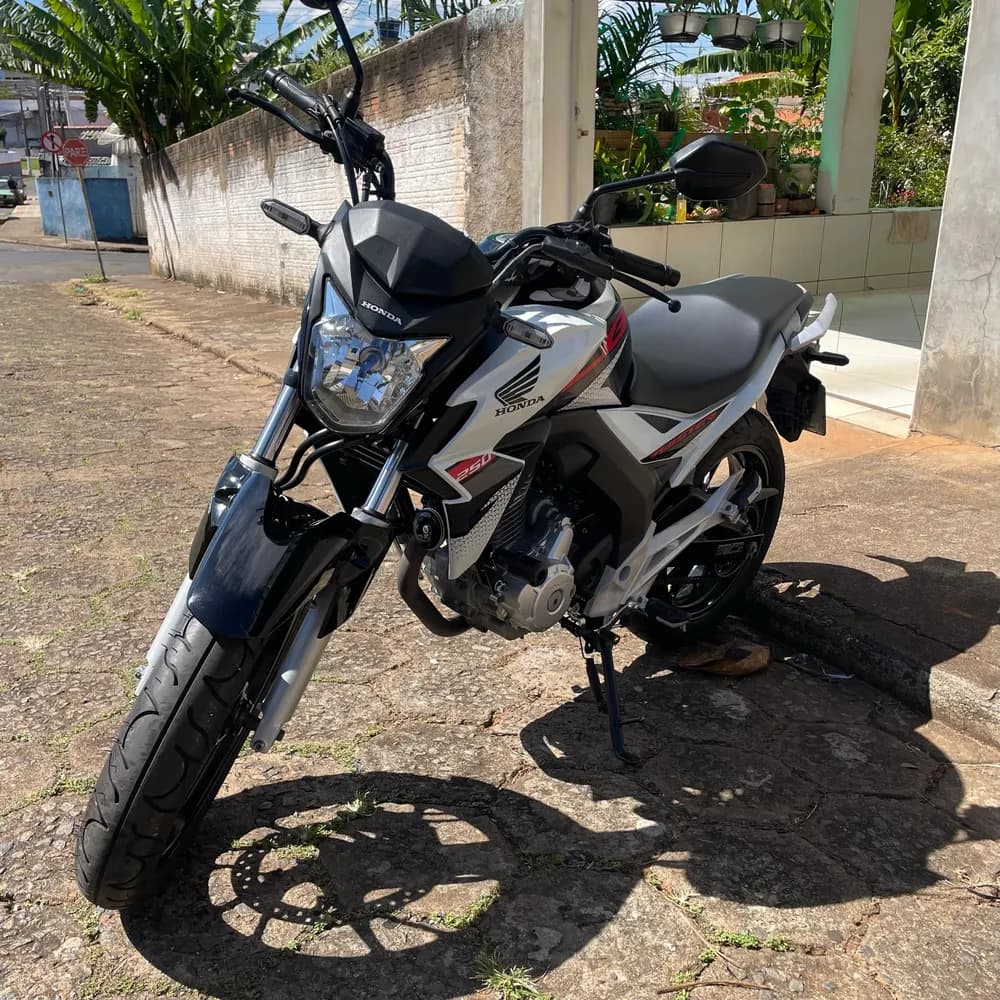 Moto branca e preta estacionada na calçada ensolarada de uma casa