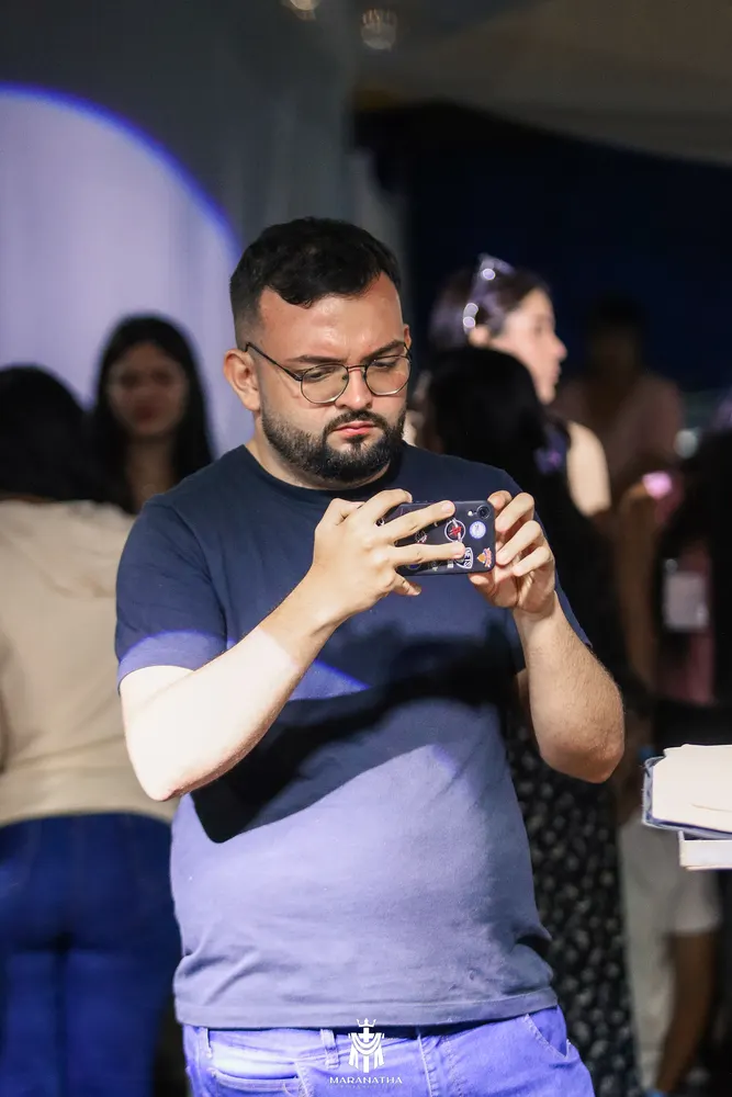 Homem de óculos segura o celular na horizontal para registrar um evento